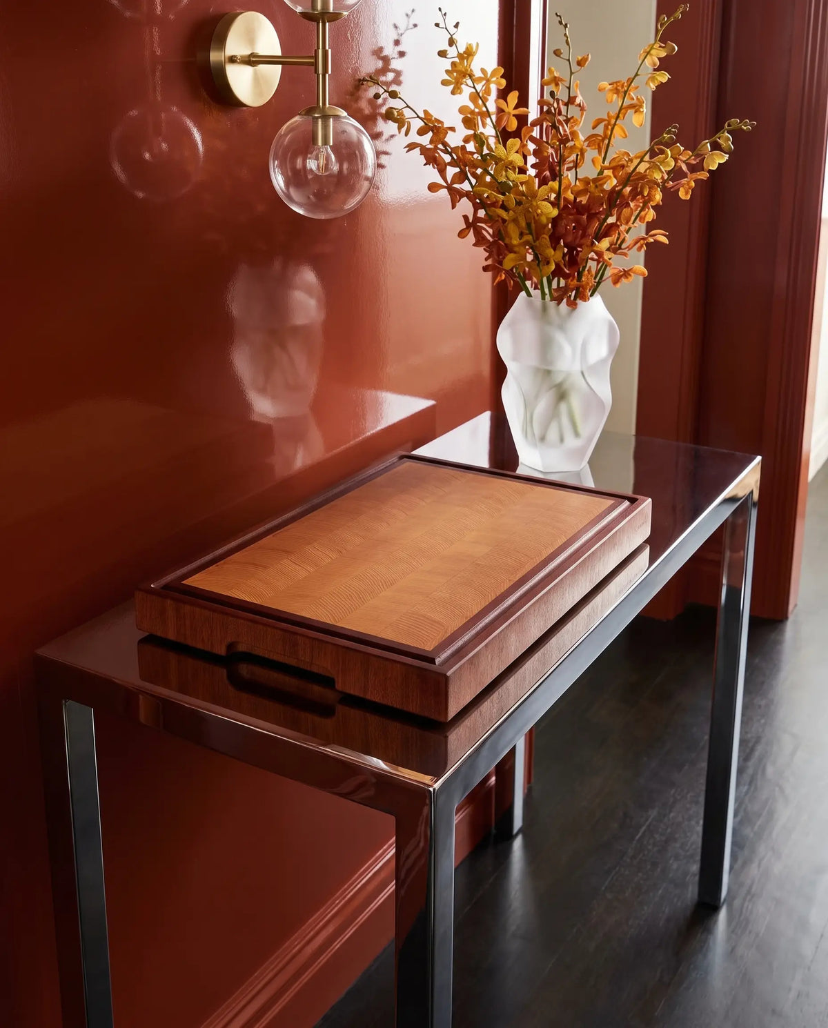 Tagliere end-grain in faggio con cornice in mogano su consolle laccata in un ingresso rosso con orchidee